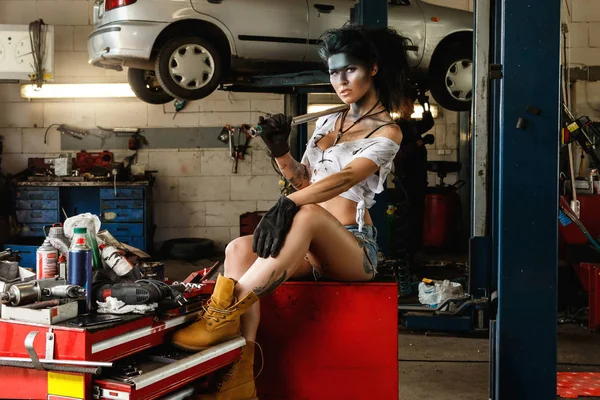 Woman mechanic in the garage with artistic makeup on her face stylized like a dirty spot