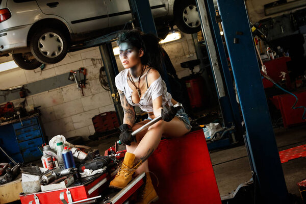 Woman mechanic in the garage with artistic makeup on her face stylized like a dirty spot