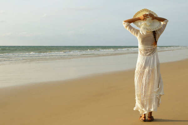 Счастливая молодая женщина в красивом белом платье гуляет по пляжу во время заката
