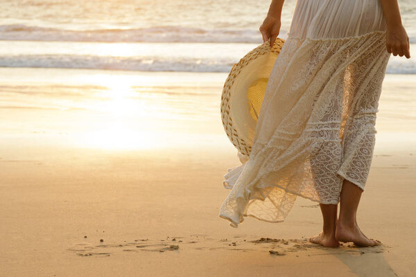 Женщина в красивом белом платье и шляпе на пляже во время заката
