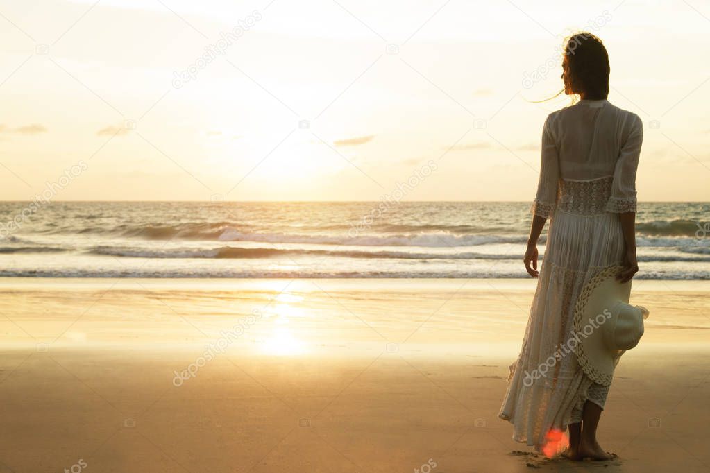Woman wearing beautiful dress and hat on beach during sunset time