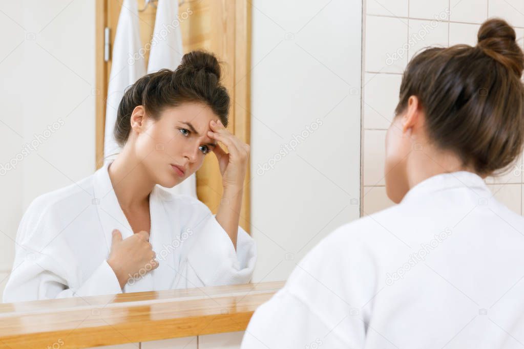 Young and sad woman with a headache looking into the mirror