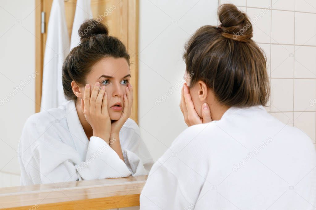 Tired woman with eyes inflammation is looking into the mirror