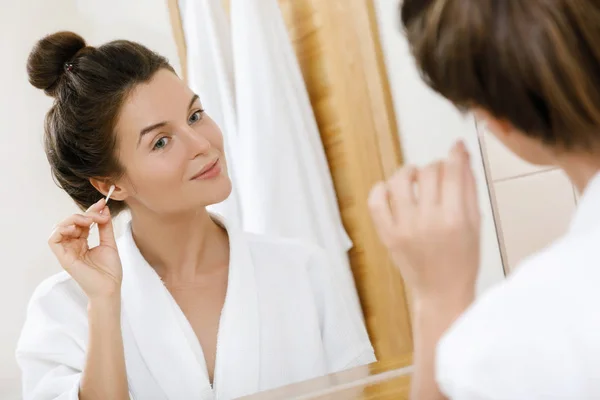 Woman cleansing her ears with a cotton swab in the bathroom