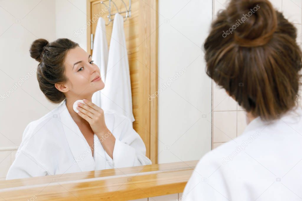 Young and beautiful woman is washing her face with lotion and cotton pads