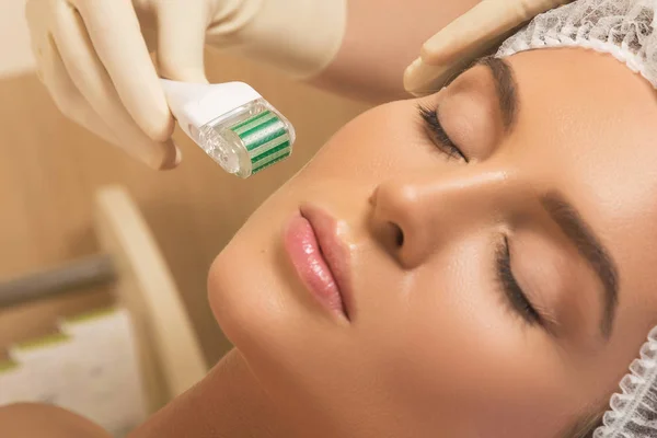 Beautiful woman in beauty salon during mesotherapy procedure.  Face microneedling treatment with a meso roller.