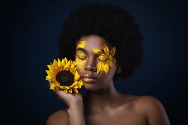 Yüzünde bir ayçiçeği ve yaratıcı makyaj ile güzel Afrikalı kadın
