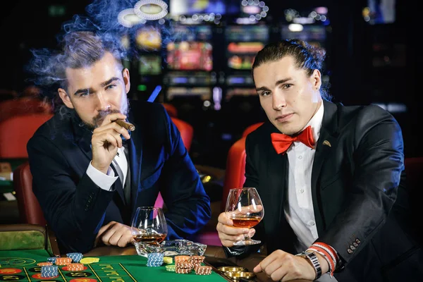 Two rich and handsome guys drinking cognac and playing roulette in the casino