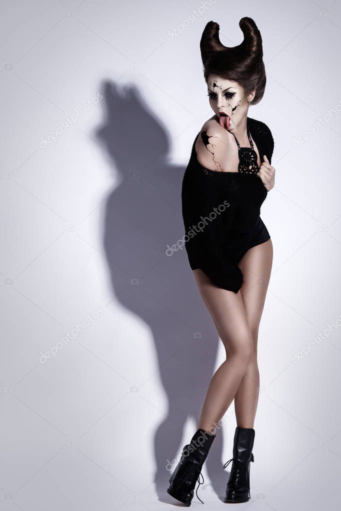 Model in creative image for Halloween. Spooky porcelain doll with horns on her head.
