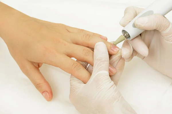 Manicure master during work. Close up of female nails and  hands with a special machine tool.