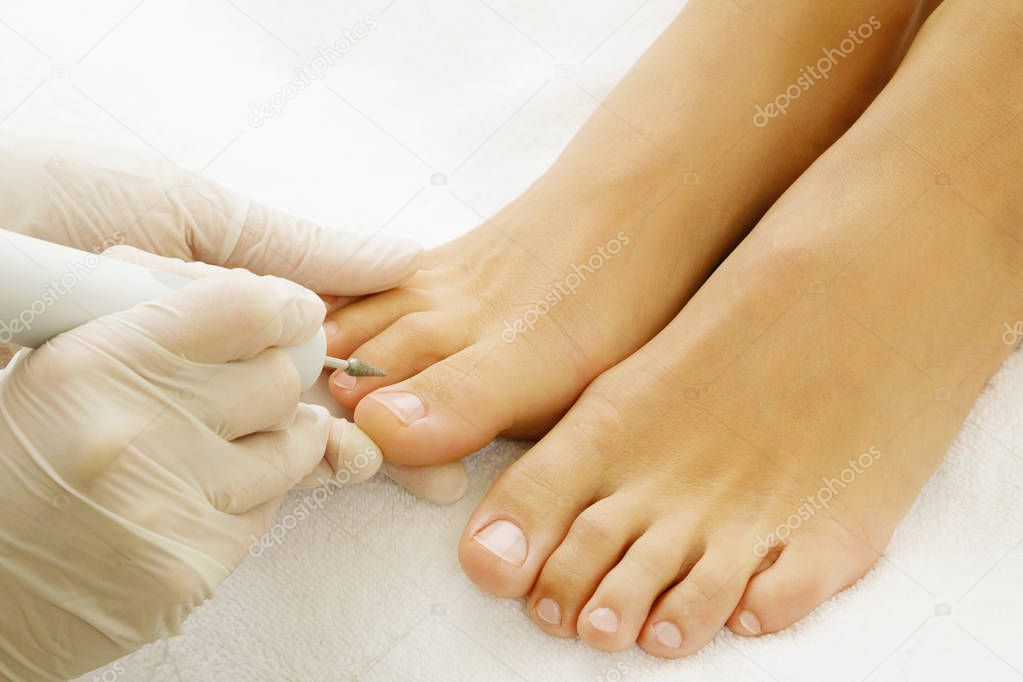 Pedicure master during work. Close up of female nails and pedicurist hands in gloves with special tool.