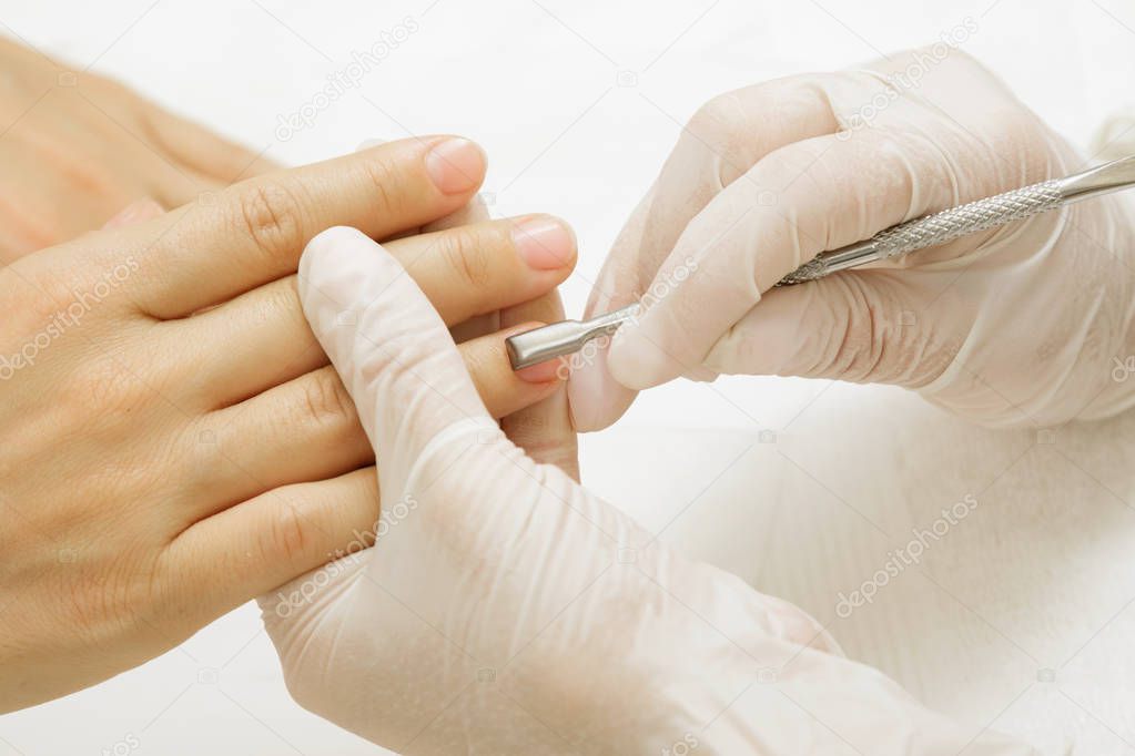 Manicure master during work. Closeup of  hands with a cuticle remover tool