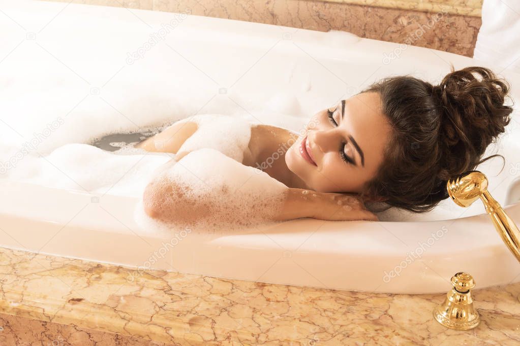 Happy and beautiful woman is taking bath with a foam in luxury apartments