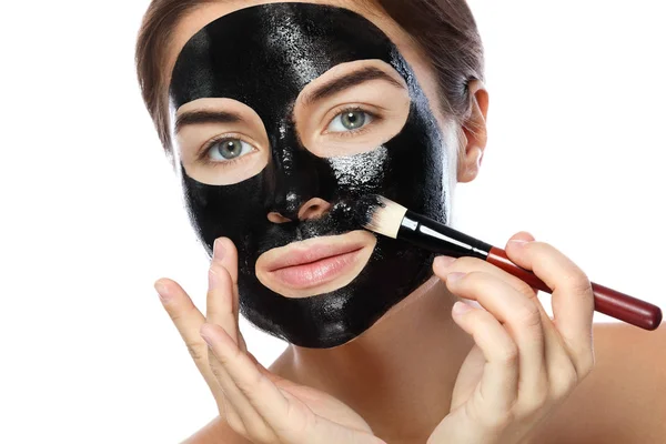 美丽的女人正在应用净化黑色面具在她的脸上白色背景 — 图库照片