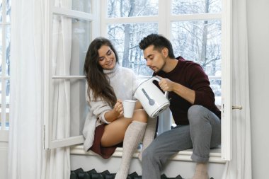 Pencere pervazına üzerinde oturan ve sıcak çay içme soğuk karlı gününde genç çift