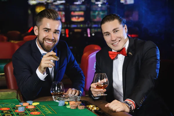 Two rich and handsome guys drinking cognac and playing roulette in the casino