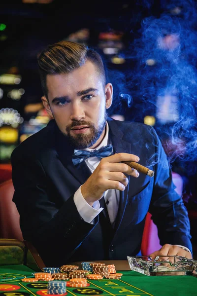 Rich handsome man smoking cigar and playing roulette in the casino