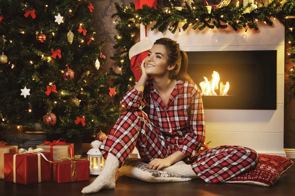 Mutlu Kadın Damalı Pijama Giymiş Noel Süslemeleri Ile Şöminenin Oturuyor — Stok fotoğraf