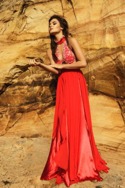 Lüks kırmızı elbise giyen ve kum uçurumlar poz güzel şehvetli kadın