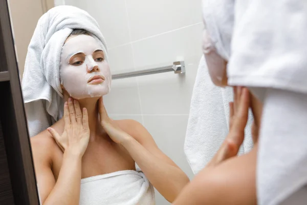 Woman in bathroom is applying facial sheet mask — Stock Photo, Image