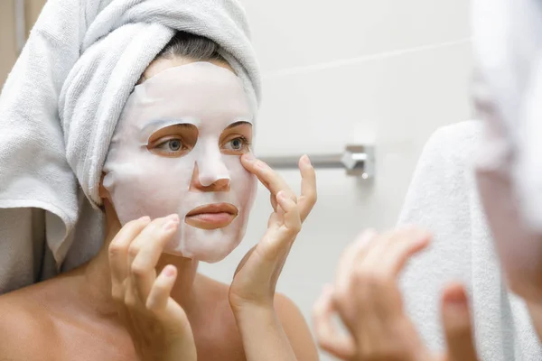 Woman in bathroom is applying facial sheet mask — Stock Photo, Image