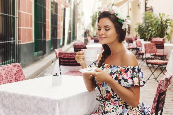 Счастливая женщина сидит в уличном кафе с чашкой горячего кофе — стоковое фото