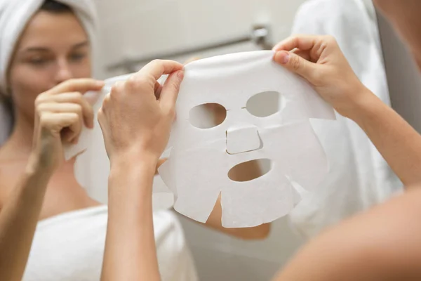 Woman in bathroom is applying facial sheet mask — Stock Photo, Image