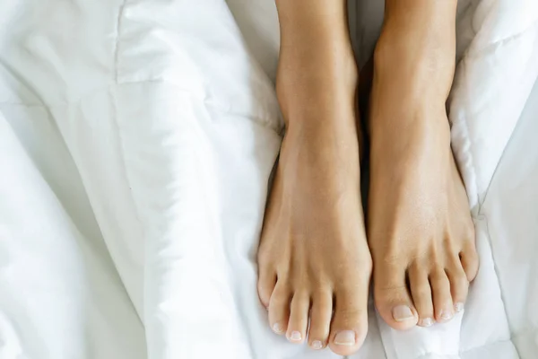 Female feet on the soft bed linen — Stock Photo, Image