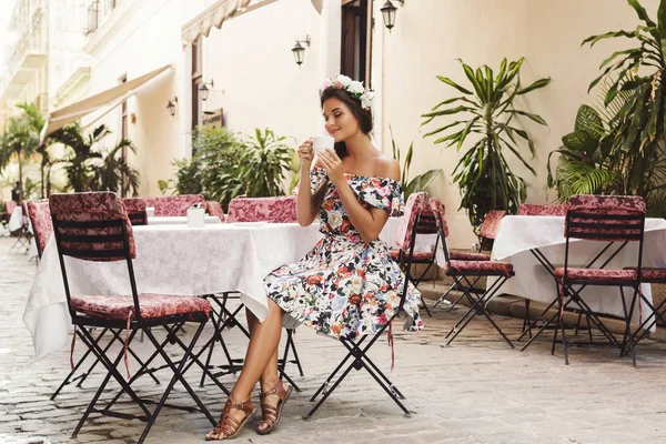 Счастливая женщина сидит в уличном кафе с чашкой горячего кофе — стоковое фото