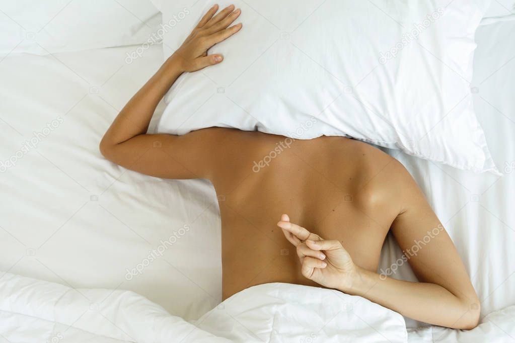 Woman lying on the bed and showing gesture of crossed fing	ers