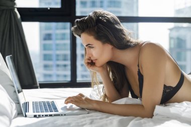 Siyah iç çamaşırı seksi kadın yatakta yalan ve dizüstü bilgisayar kullanarak