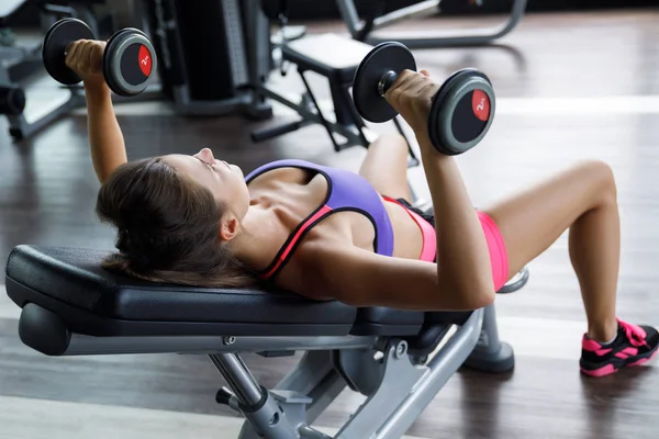 女人在健身房里用哑铃锻炼。斜线工作台压机. — 图库照片