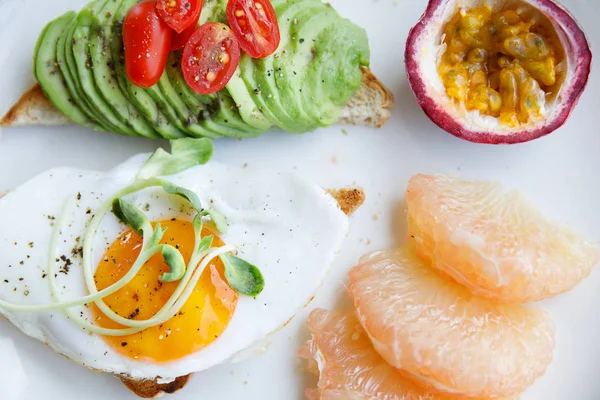 Rostat bröd med stekt ägg avokado och frukt till frukost — Stockfoto