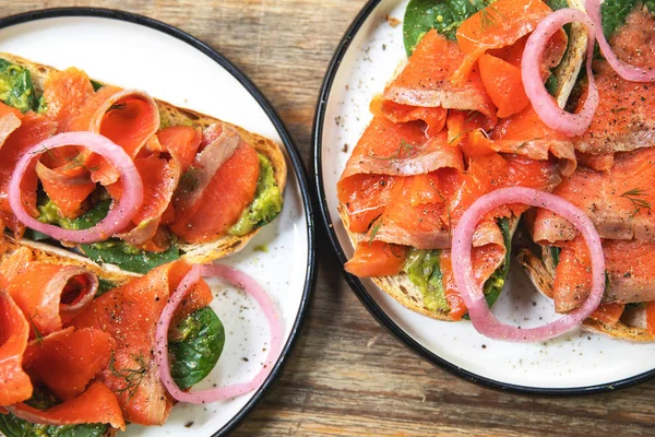 Delicious toasts with smoked salmon, avocado and basil leaves — Stock Photo, Image