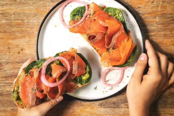 Female hands and delicious toasts with a smoked salmon, avocado — Stock Photo, Image