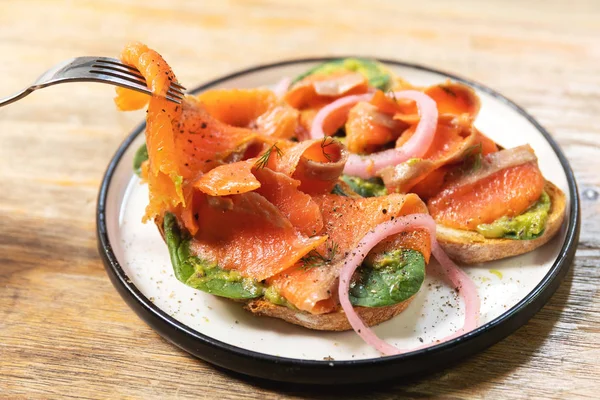 Delicious toasts with smoked salmon, avocado and basil leaves — Stock Photo, Image