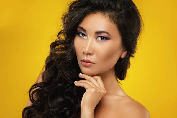 Asiatische Frau mit einem schönen lockigen Haar und Make-up auf gelb ba — Stockfoto