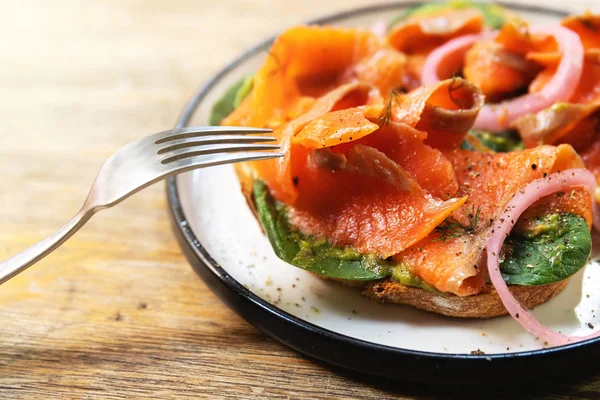 Läckra rostat bröd med rökt lax, avokado och basilikablad — Stockfoto