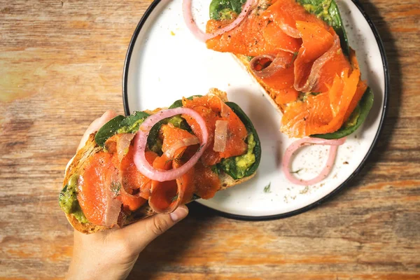 Female hands and delicious toasts with a smoked salmon, avocado — Stock Photo, Image