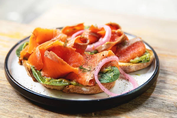 Läckra rostat bröd med rökt lax, avokado och basilikablad — Stockfoto