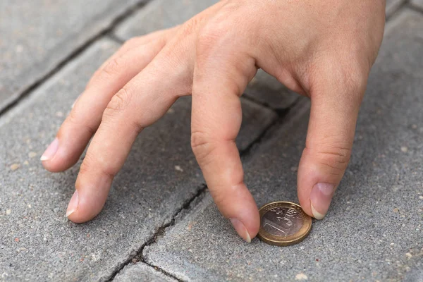 Female hand picking one euro coin from the ground