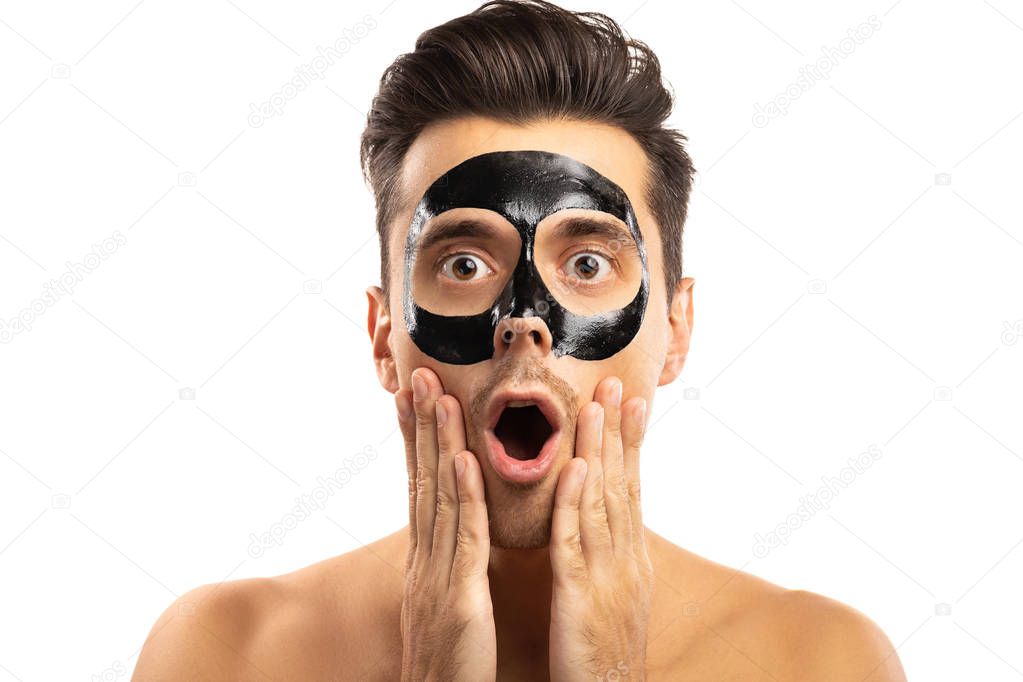 Young guy with a black charcoal mask on his face on white backgr