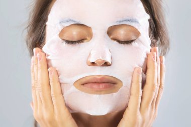 Yüzünde bir çarşaf nemlendirici maske ile kadın gra izole