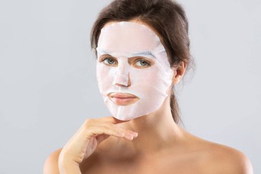 Yüzünde bir çarşaf nemlendirici maske ile kadın gra izole