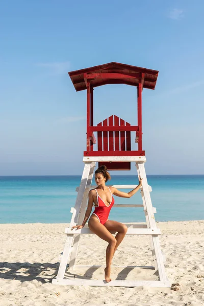 Mulher sexy em maiô vermelho posando ao lado de uma torre de salva-vidas — Fotografia de Stock