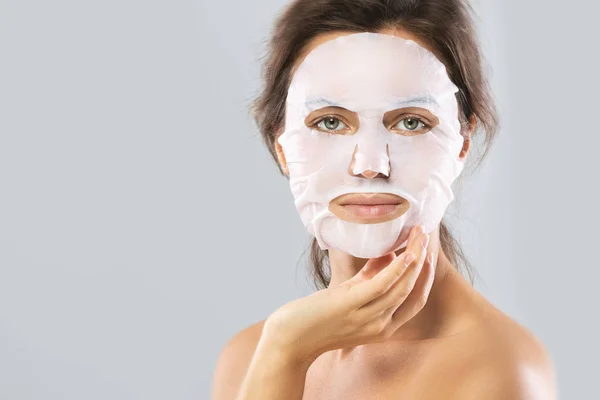 Mulher com uma máscara hidratante folha em seu rosto isolado em gra — Fotografia de Stock