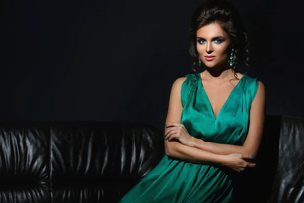 性感的女人在美丽的绿色礼服在皮革沙发上摆姿势 — 图库照片