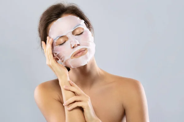 Mulher com uma máscara hidratante folha em seu rosto isolado em gra — Fotografia de Stock