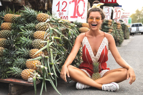 Young and happy woman with a pile of pineapples on the local Tha