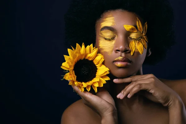 Afrykańska kobieta ze słonecznikiem i kreatywnym makijażem na twarzy — Zdjęcie stockowe